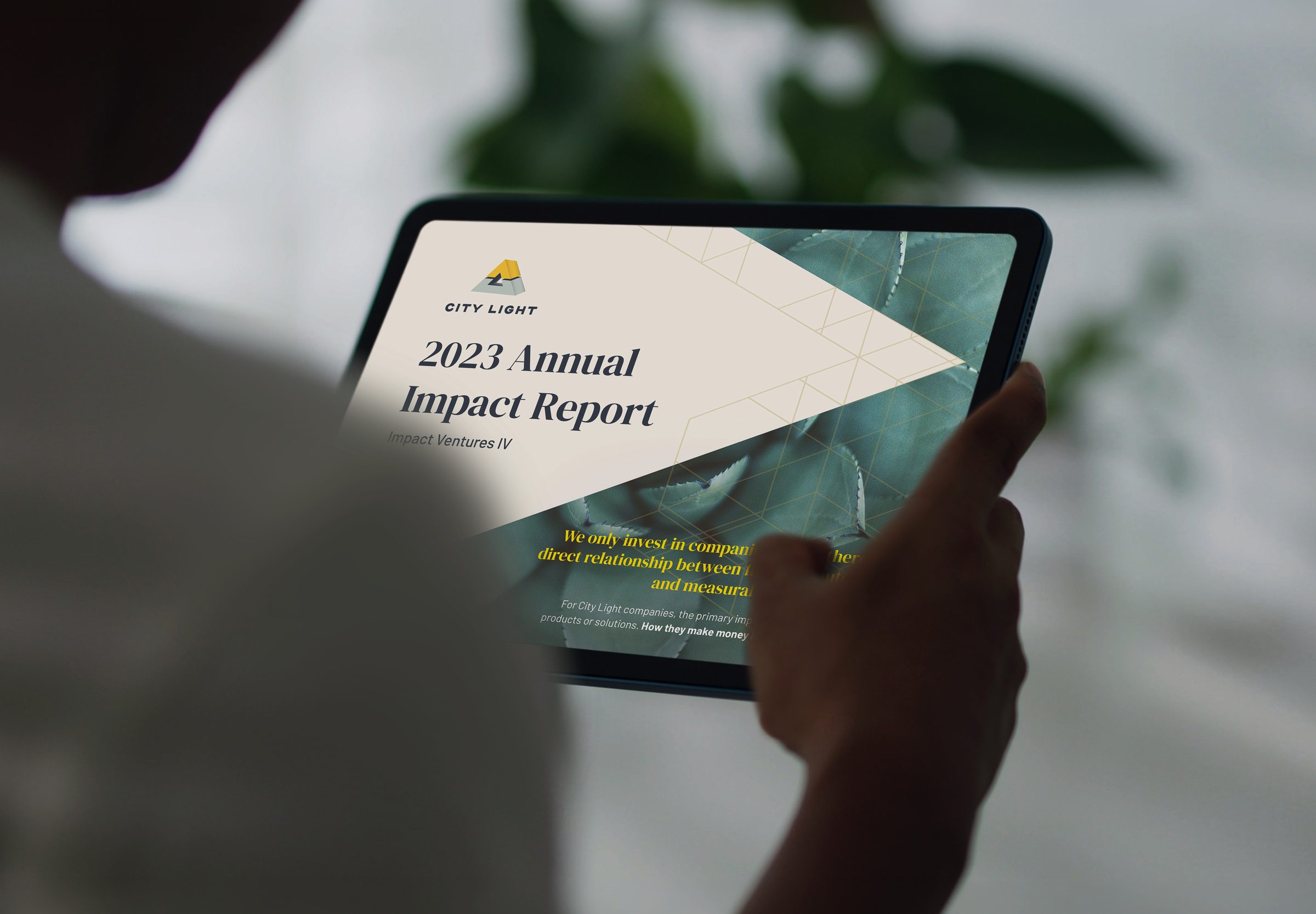 The 2023 Annual Impact Report cover open on a tablet, held in someone's hands